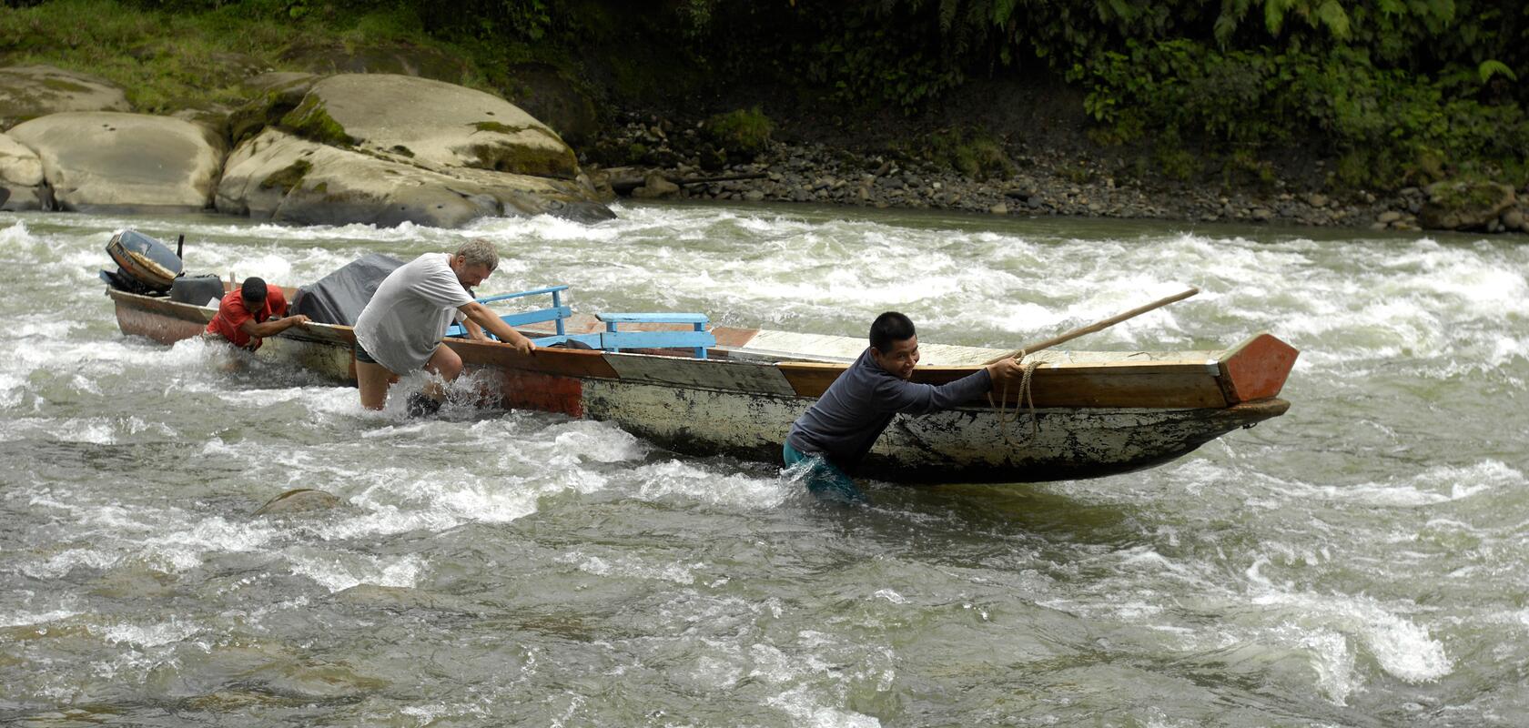 Drei Männer stossen ein Boot über eine Stromschnelle. Das Bild steht symbolisch  für den Weg zum Einsatz, den neue Fachleute von Comundo begehen.